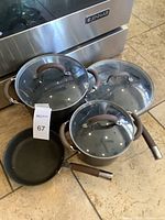 Set of brown Circulon cookware including three pots/pans with handles and two glass lids.