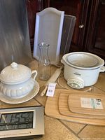 Overall kitchen items including crockpot, ceramic dish, cutting boards, clock, carafe, and serving trays.