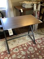 Photo of small desk showing brown particle board top and black metal leg frame on patterned carpet.