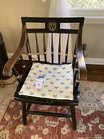 Full view of black wooden chair with Harvard Law School seal and cream cushion with printed eagle symbols, placed on a patterned rug in front of a window.