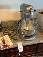 Full view of mixer on countertop with bowl attached, attachments and manual laid out