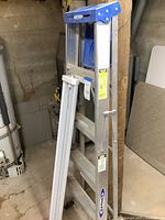 Full view of Werner aluminum ladder standing upright showing blue plastic top and aluminum steps and frame.