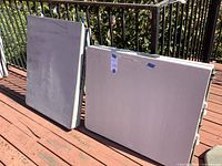 Two folded Lifetime folding tables leaned against railing on wooden deck, showing front top surfaces which are marked and stained.