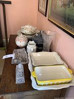 Overall view of ceramic and glass serving dishes, flower vase, and metal corn holders arranged on wooden table.