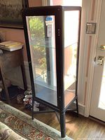 Full front view of the tall grey metal display case with glass shelves, showing its slim profile and door.