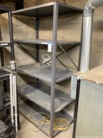 Full view of the metal storage rack showing four gray perforated shelves in a basement setting. Rack is dusty and shows signs of wear.