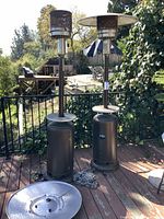 Two full view outdoor patio heaters on a deck with surrounding greenery. Both heaters show rust at base, measuring about 86" tall. One heater missing top cover.