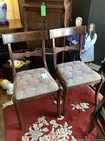Pair of antique wooden chairs with upholstered seats on a patterned red carpet, showing overall condition and design.