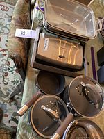 Photo showing electric Griddler panini press, Cuisinart chafing dish tray, and multiple pots and pans with lids placed on a table.