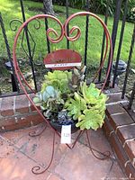 Front view of the heart-shaped metal planter with succulent plants and a metal "welcome" sign inside a black round container.