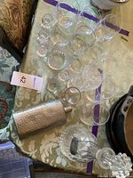 Full view of glassware set arranged on table including Scotch decanter with stopper, metal flask, wine glasses, and small cups.