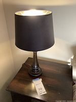 Full view of one table lamp illuminated on a wooden side table, showing overall shape, shade, and base.
