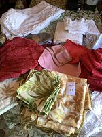 Assorted folded table linens in various colors including white, red, pink, green, and beige, showing some creases and used condition.