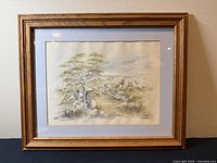 Framed artwork print hanging on wall showing wooden frame and signed landscape print.