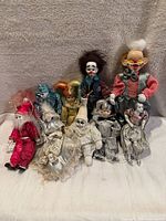 Lot of 10 vintage porcelain face clown and doll figurines arranged on a grey backdrop, showing details of their faces and costumes.