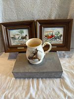 Vintage Sadler bone China mug with a horse head image on front placed in front of two wooden framed metal paintings featuring horse and carriage scenes, signed Milord and Calesa.