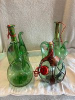 Four vintage hand-blown glass decanters including three green with ice chambers and one clear with leather and metal details, all with stoppers tied with red string.