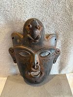 Front view of black clay pottery mask showing detailed carvings and frog figure on forehead.
