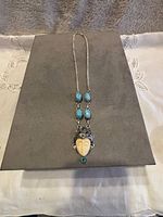 Full view of the vintage Bali ivory color goddess pendant necklace with turquoise stones on display board