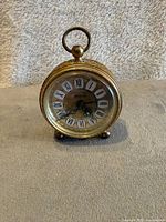 Front view showing round gilded floral filigree metal clock with Roman numeral dial, turquoise accents, and acrylic face cover.