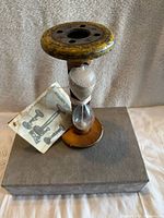 Front view of vintage bobbin timer hourglass on wooden base with original manual. Manual shows wear and age.