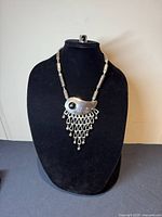 Full view of the brutalist bib necklace displayed on a black bust stand, showing the unique abstract bib pendant with black onyx stone and silver fringe elements.