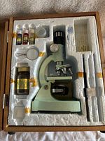 Top view of microscope and accessories set inside molded foam in original wooden box.