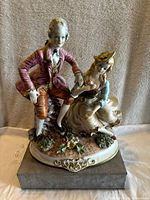 Front view of Victorian couple porcelain figurine on stand, showing posed man and woman in period dress with floral decorated base.