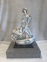 Front view of the vintage porcelain figurine showing the lady in a blue floral dress with cart full of flowers, mounted on a black base