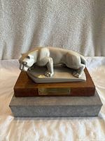 Front view of gray Nittany Lion statue on wooden base with brass plaque