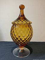 Full view of vintage honey amber Empoli apothecary jar with lid on clear pedestal base on black surface