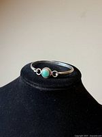 Side angle of vintage sterling silver hinged bangle bracelet showing the round malachite stone in the center with loops on each side, resting on a black display stand.