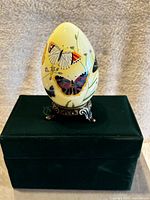 Front view of the glass egg on metal stand, showing multiple butterflies painted on yellow background.
