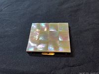 Closed view of the vintage powder compact showing the iridescent mother of pearl checkerboard top design.