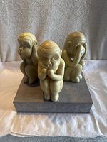 Front view of three beige resin monkey figurines on a gray base, each monkey has a different pose covering ears, mouth, or eyes.