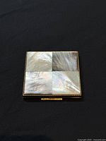 Front of vintage gold-tone powder compact decorated with four square mother of pearl panels in a checkerboard pattern.