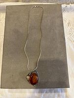 Full view of the silver necklace with Baltic amber pendant on a gray background.