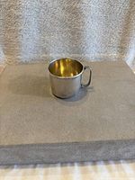 Side view of the vintage sterling silver baby cup showing polished shiny surface and handle