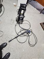 Full view of the AR Blue Clean power washer unit with hose and wand laid in front on a concrete floor.