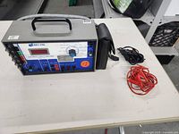 Photo of Bio-Tek Electrical Safety Analyzer on table with attached cables and separate red and black test leads beside it.