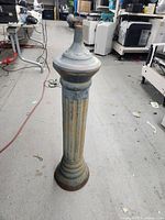Cast iron weather vane post standing upright on concrete floor showing fluted column and circular base with rust and wear.