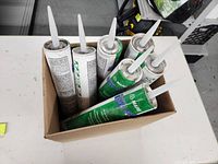 Seven unopened tubes of adhesive caulk with pointed nozzles inside a cardboard box.