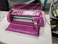 Purple Cricut Expression electronic cutting machine on a table, blade carriage visible.