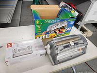 Xyron EZ Laminator hand-operated device next to its original packaging box with promotional design and text.