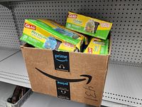 Box containing multiple packages of Glad trash bags including recycling and clear trash bags with yellow and green packaging.