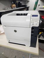 Front view of white and gray HP LaserJet 600 M602 printer showing main body and control keypad area.