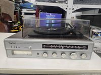 Full front view of the Kings Point stereo showing the record turntable on top inside a clear dust cover, knobs and AM/FM tuning scale.