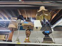 Photo showing five lamps on a shelf with varied bases and fabric shades in beige, brown, black, and yellow.