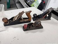 Three handheld woodworking planers arranged on a white surface showing handles and bodies.