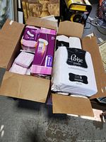 Two open boxes with multiple packages of Poise brand pads inside. One pack in white packaging with black label visible, another pack mostly pink and purple packaging.